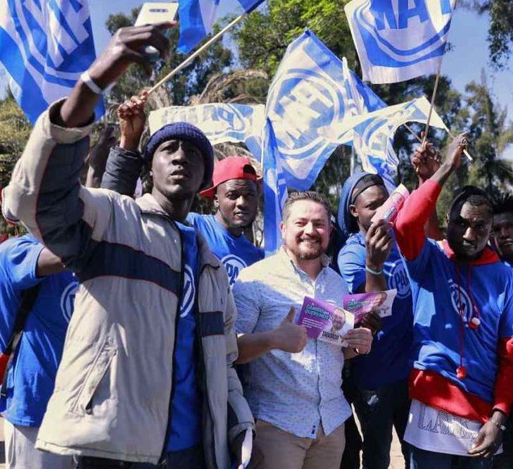 Francisco Romo, un añejo militante del PAN, posa con migrantes haitianos acarreados para evento de Santiago Taboada